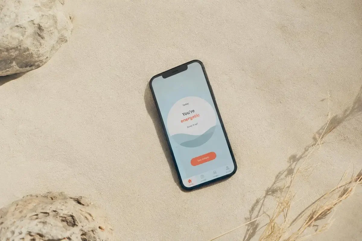 故事专栏《把一整片海装进口袋：App 背后的七个月》配图 - 故事专栏配图：细沙上的一部手机显示湖蓝色极简界面，杂志风海报